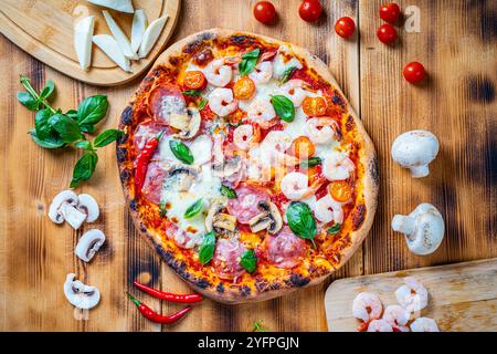 Pizza with two types of toppings, one half paperoni with mushrooms, the other tomatoes and shrimps with cheese. Pizza on a wooden table with ingredien Stock Photo