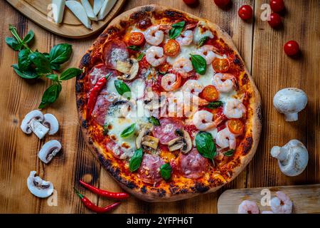 Pizza with two types of toppings, one half paperoni with mushrooms, the other tomatoes and shrimps with cheese. Pizza on a wooden table with ingredien Stock Photo