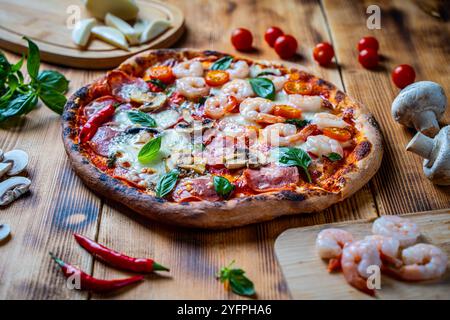 Pizza with two types of toppings, one half paperoni with mushrooms, the other tomatoes and shrimps with cheese. Pizza on a wooden table with ingredien Stock Photo