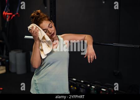 A woman is wiping her face with a towel in a gym. She is wearing a green tank top and she is tired Stock Photo