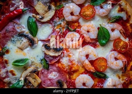 Pizza with two types of toppings: one half of pepperoni with mushrooms, the other with tomatoes and shrimp with cheese. Background with pizza texture. Stock Photo