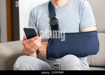 Close up of man hands with broken arm wearing sling using smart phone at home Stock Photo