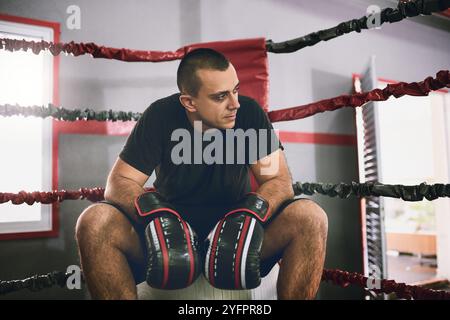 Man, tired boxer and fitness in ring at gym, sports fail and mma athlete for training defeat. Male person, exhausted sportsman and rest in corner for Stock Photo