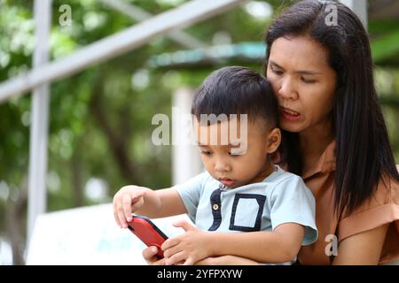 A caring mother shares a moment with her son as they engage with a smartphone outdoors, highlighting the bond of family and technology in a natural se Stock Photo