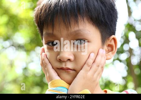 A thoughtful boy in a serene natural setting displays deep emotions. His gentle expression and contemplative posture convey a sense of innocence and i Stock Photo