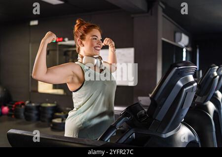 Happy athletic woman celebrating workout success with victory gesture on treadmill in modern gym Stock Photo