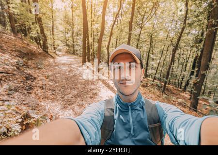 Smiling young man taking a selfie while hiking solo in a scenic forest park Stock Photo