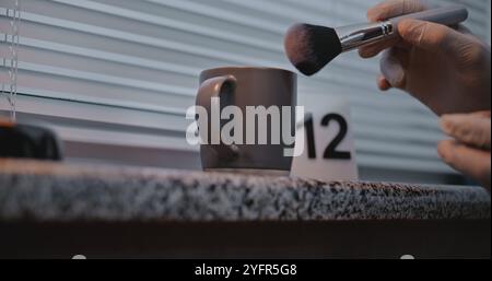 Murder or robbery case: Close up of unrecognizable criminalist searching fingerprints on cup belonging to victim using brush and magnetic powder. Forensic scientist works with evidence at crime scene. Stock Photo