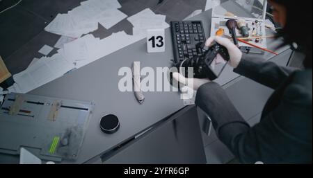 Robbery or murder case: Top view on female criminalist taking photos of knife with professional camera. Numbered marker stands next to murder weapon evidence. Forensic scientist works at crime scene Stock Photo