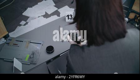 Robbery or murder case: Top view on female criminalist taking photos of knife with professional camera. Numbered marker stands next to murder weapon evidence. Forensic scientist works at crime scene Stock Photo
