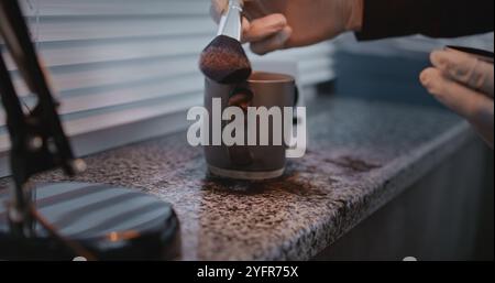 Murder or robbery case: Close up of unrecognizable forensic scientist finding fingerprints on cup belonging to victim using brush and magnetic powder. Criminalist works with evidence at crime scene. Stock Photo