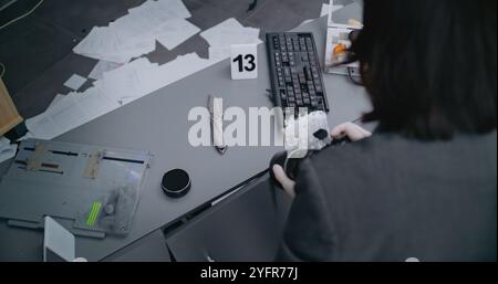 Robbery or murder case: Top view on female criminalist taking photos of knife with professional camera. Numbered marker stands next to murder weapon evidence. Forensic scientist works at crime scene Stock Photo