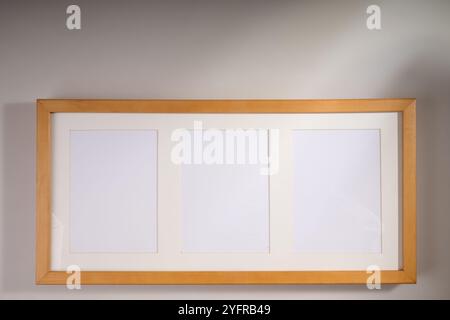 Wooden frame for three pictures on white wall with light and shadows Stock Photo
