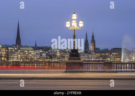 View from the Lombardsbruecke at blue hour with light traces of cars on the Inner Alster Lake with Alster fountain, town hall and Jungfernstieg, Hambu Stock Photo
