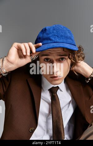 A handsome young man wearing a brown suit and blue cap strikes a contemplative pose in a studio space. Stock Photo