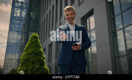 Happy smiling Caucasian businessman in city old senior mature business employer retired man entrepreneur with mobile phone using smartphone showing Stock Photo