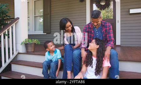 Portrait Of Smiling Family Sitting On Steps Of Suburban Home Stock Photo