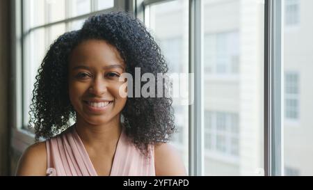 Head And Shoulders Portrait Of Smiling Young Businesswoman Standing By Window In Office Stock Photo