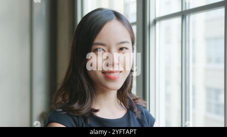 Head And Shoulders Portrait Of Smiling Young Businesswoman Standing By Window In Office Stock Photo