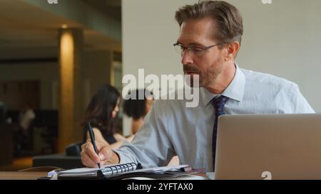 Mature Businessman In Informal Seating Area Of Modern Office Working On Laptop Stock Photo