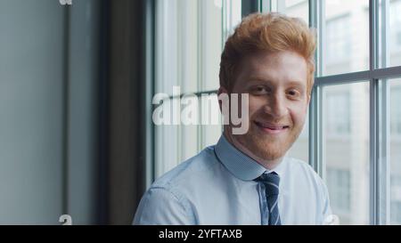 Head And Shoulders Portrait Of Smiling Young Businessman Standing By Window In Office Stock Photo