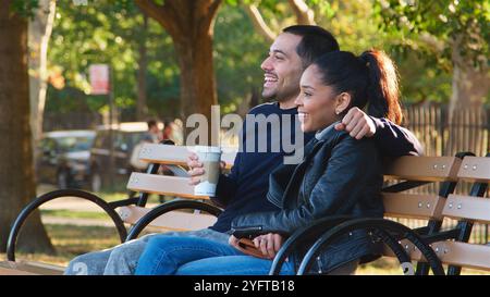 Loving Young Couple Sitting Outdoors On Park Bench With Takeaway Coffee Stock Photo