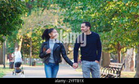 Loving Young Couple Outdoors Walking Through Park Holding Hands Together Stock Photo