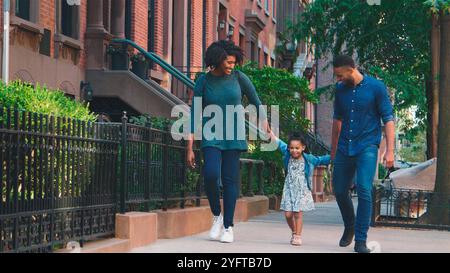 Family Shot With Parents Holding Hands With Daughter As They Walk Along Street In New York City Stock Photo