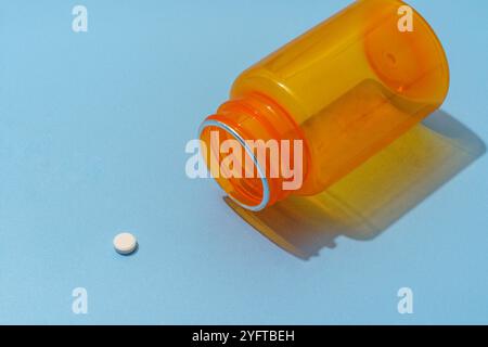 Orange Plastic Pill Bottle lies on its side with a White Medication Tablet on Blue Background Stock Photo
