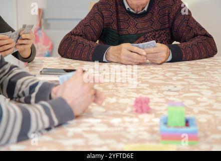 A group of people gather around a table playing cards, a casual game with family or friends, promoting social interaction Stock Photo