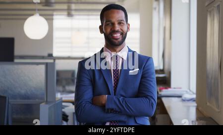 Portrait Of Smiling Businessman With Folded Arms Wearing Suit Working In Empty Open Plan Office Stock Photo