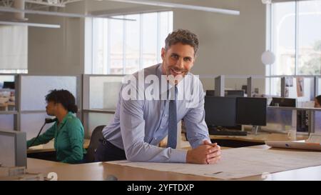 Portrait Of Mature Male Architect In Modern Open Plan Office Studying Building Plans Or Drawings Stock Photo