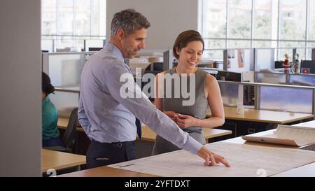 Male And Female Architects Meeting In Modern Open Plan Office Studying Building Plans Or Drawings Stock Photo