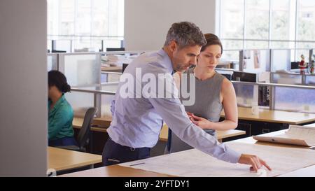 Male And Female Architects Meeting In Modern Open Plan Office Studying Building Plans Or Drawings Stock Photo