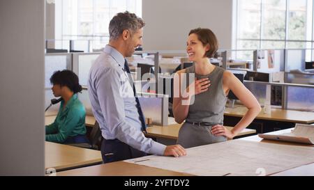 Male And Female Architects Meeting In Modern Open Plan Office Studying Building Plans Or Drawings Stock Photo