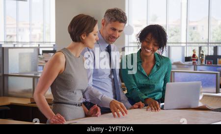 Male And Female Architects Meeting In Modern Open Plan Office Studying Building Plans Or Drawings Stock Photo