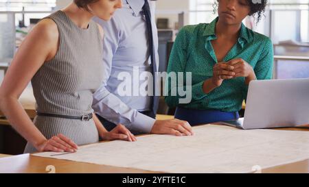 Close Up Of Male And Female Architects Meeting In Office Studying Building Plans Or Drawings Stock Photo