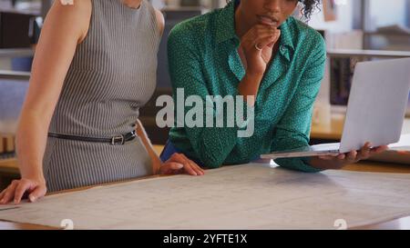 Close Up Of Two Female Architects Meeting In Office With Laptop Studying Building Plans Or Drawings Stock Photo