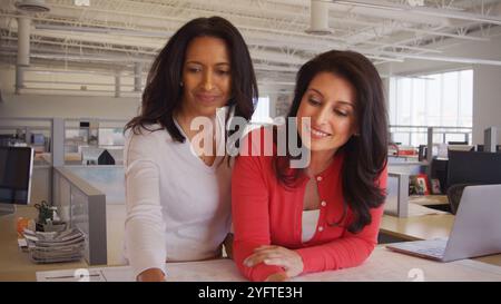 Two Mature Female Architects Meeting In Modern Open Plan Office Studying Building Plans Or Drawings Stock Photo