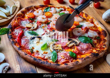 Pizza with two types of toppings: one half with shrimp and tomatoes, the other with pepperoni and mushrooms. Pizza is cut with a special roller knife. High quality photo Stock Photo