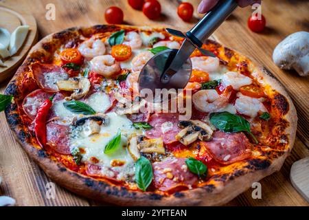 Pizza with two types of toppings: one half with shrimp and tomatoes, the other with pepperoni and mushrooms. Pizza is cut with a special roller knife. High quality photo Stock Photo