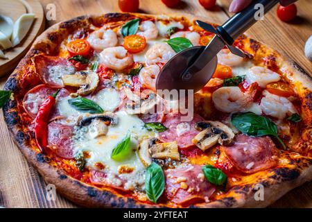 Pizza with two types of toppings: one half with shrimp and tomatoes, the other with pepperoni and mushrooms. Pizza is cut with a special roller knife. High quality photo Stock Photo