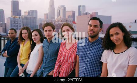 Portrait Of Friends Standing In A Line On Rooftop Terrace For Party With City Skyline In Background Stock Photo