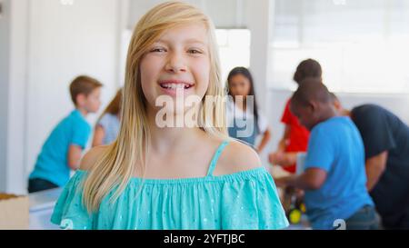Portrait Of Smiling Female Student In School Computer Class With Teacher And Pupils In Background Stock Photo