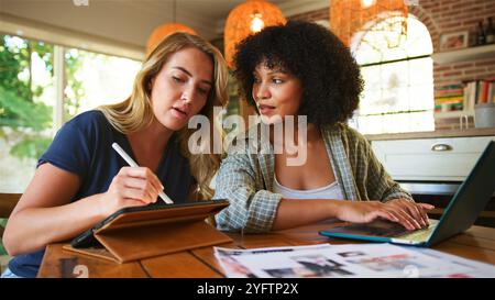 Two women engage in a thoughtful discussion about their creative project while working together in a cozy home office environment. One woman writes on Stock Photo