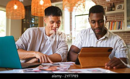Two individuals sit at a bright table engaging in a collaborative effort. One person points to printed materials while the other takes notes on a tabl Stock Photo