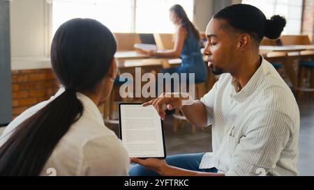 Two Young Businesspeople With Digital Tablet Meeting In Office With Colleagues In Background Stock Photo