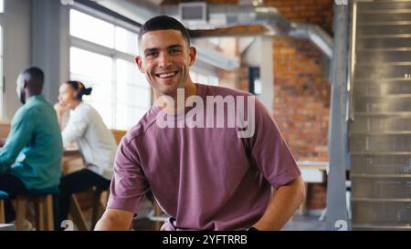 Portrait Of Young Smiling Businessman Working In Modern Open Office With Colleagues In Background Stock Photo