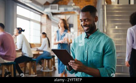 Smiling Businessman Using Digital Tablet Working In Busy Modern Open Plan Office Stock Photo