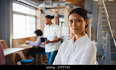 Portrait Of Serious Young Businesswoman Working In Open Plan Office With Colleagues In Background Stock Photo